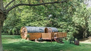 A wooden cabin with a covered porch and a small deck, surrounded by lush greenery. - Domaine de Marguerite (Janvry)