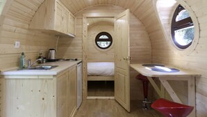 A small, wooden cabin with a kitchenette, a single bed, and a round window. - Domaine de Marguerite (Janvry)