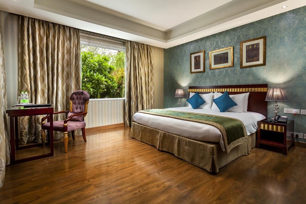 A hotel room with a large bed, a desk, a chair, and a window with curtains.