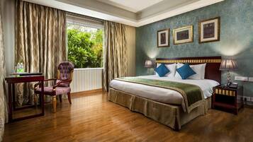A hotel room with a large bed, a desk, a chair, and a window with curtains.