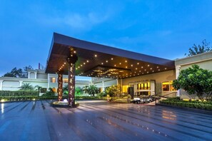 Ein moderner Hotelzugang mit überdachtem Gang, einer Fontäne und einem gepflegten Garten.