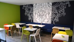A dining area with colorful chairs and tables, a large black and white mural on the wall, and a green accent wall. - Hoteleco Sud (Le Passage)