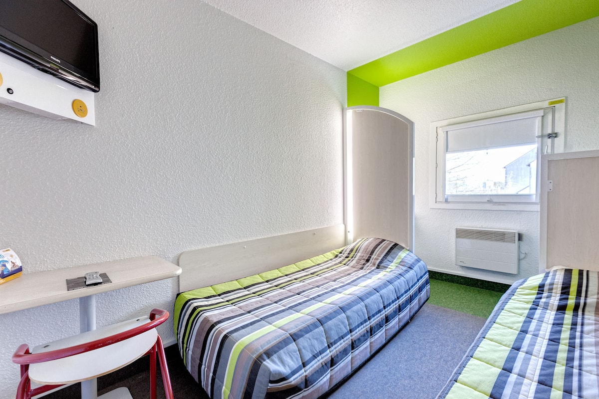 A room with two beds, a desk, a chair, a television, and a window.