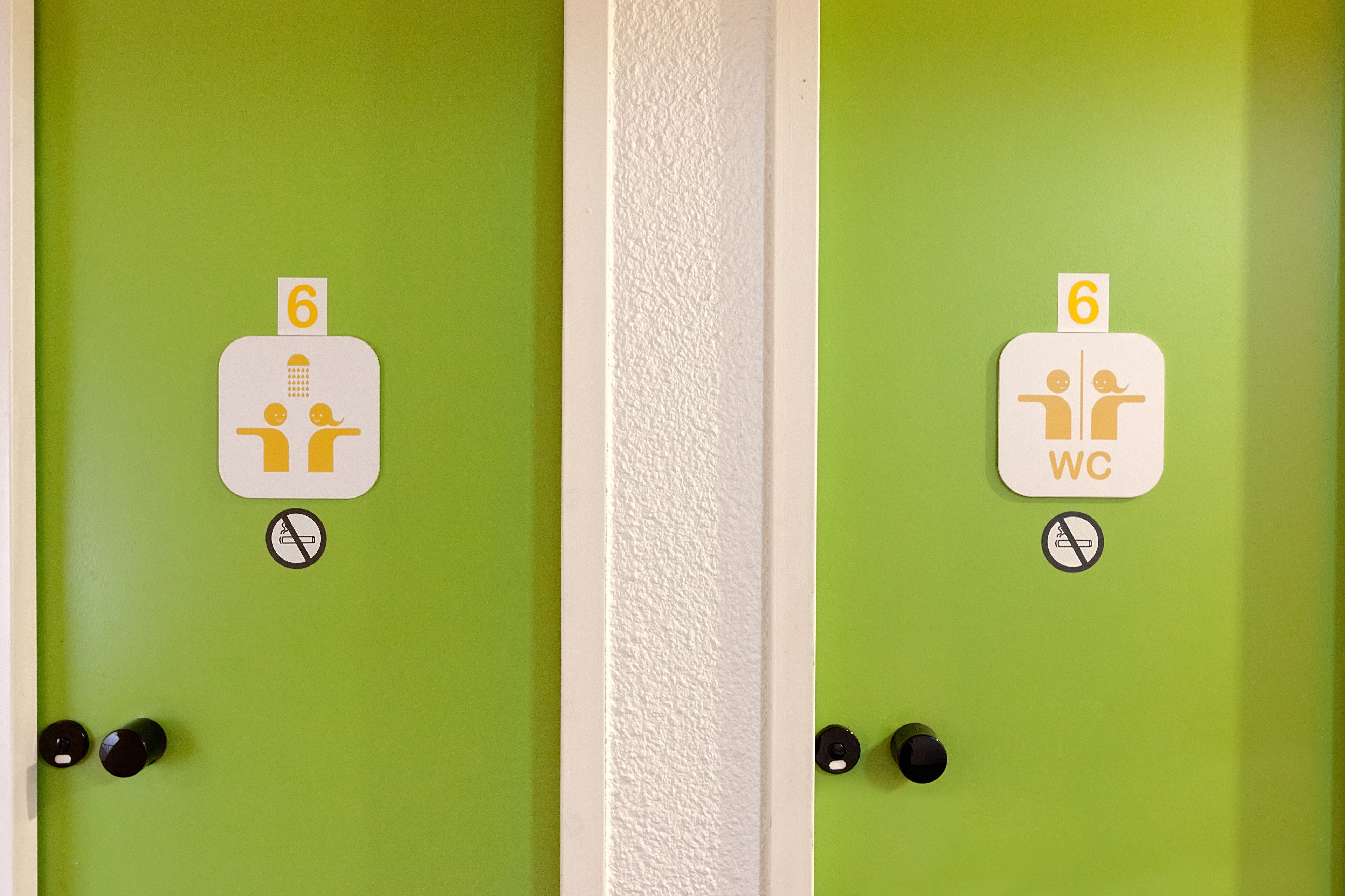 To grønne døre med hvide skilte, der viser værelsesnumre 6 og et toilet.