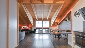 Una cocina moderna con vigas de madera, una zona de comedor con mesa y sillas, y una chimenea encendida.
