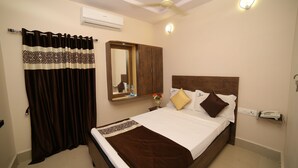 A bedroom with a bed, a mirror, a ceiling fan, and an air conditioning unit. - Hotel Bhavani Grand (Nidadavolu)