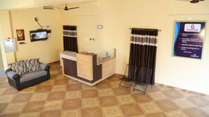 A reception area with a sofa, a reception desk, a television, and a ceiling fan. - Hotel Bhavani Grand (Nidadavolu)