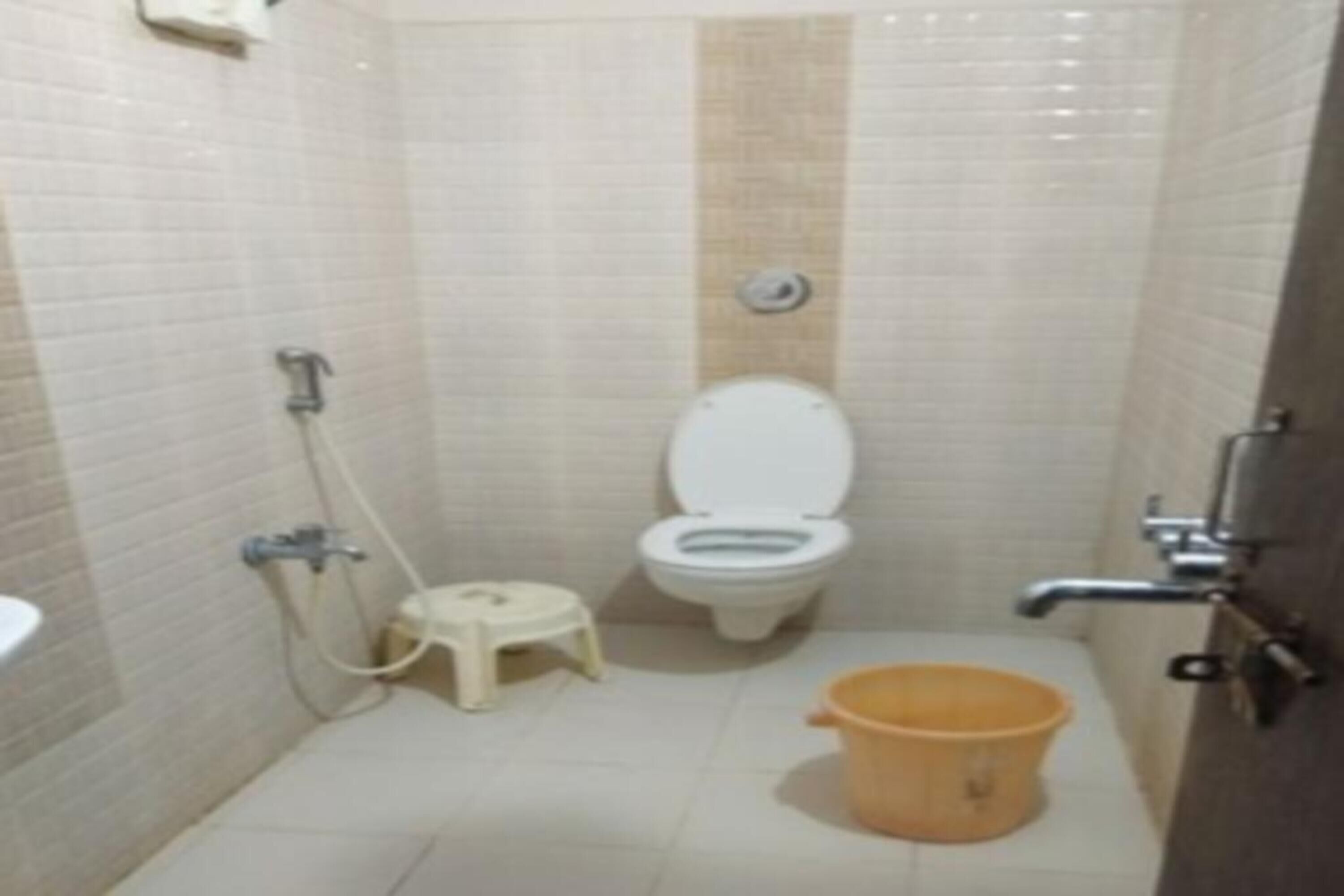 A small, tiled bathroom with a toilet, a shower, a sink, and a small stool.