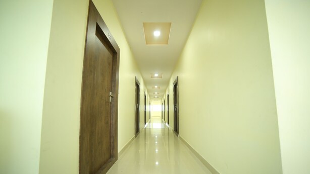 A long, narrow hallway with wooden doors on either side and a series of recessed lights on the ceiling. - Hotel Bhavani Grand (Nidadavolu)