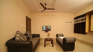 A living room with two sofas, a small table with a vase, a ceiling fan, and a television on the wall. - Hotel Bhavani Grand (Nidadavolu)