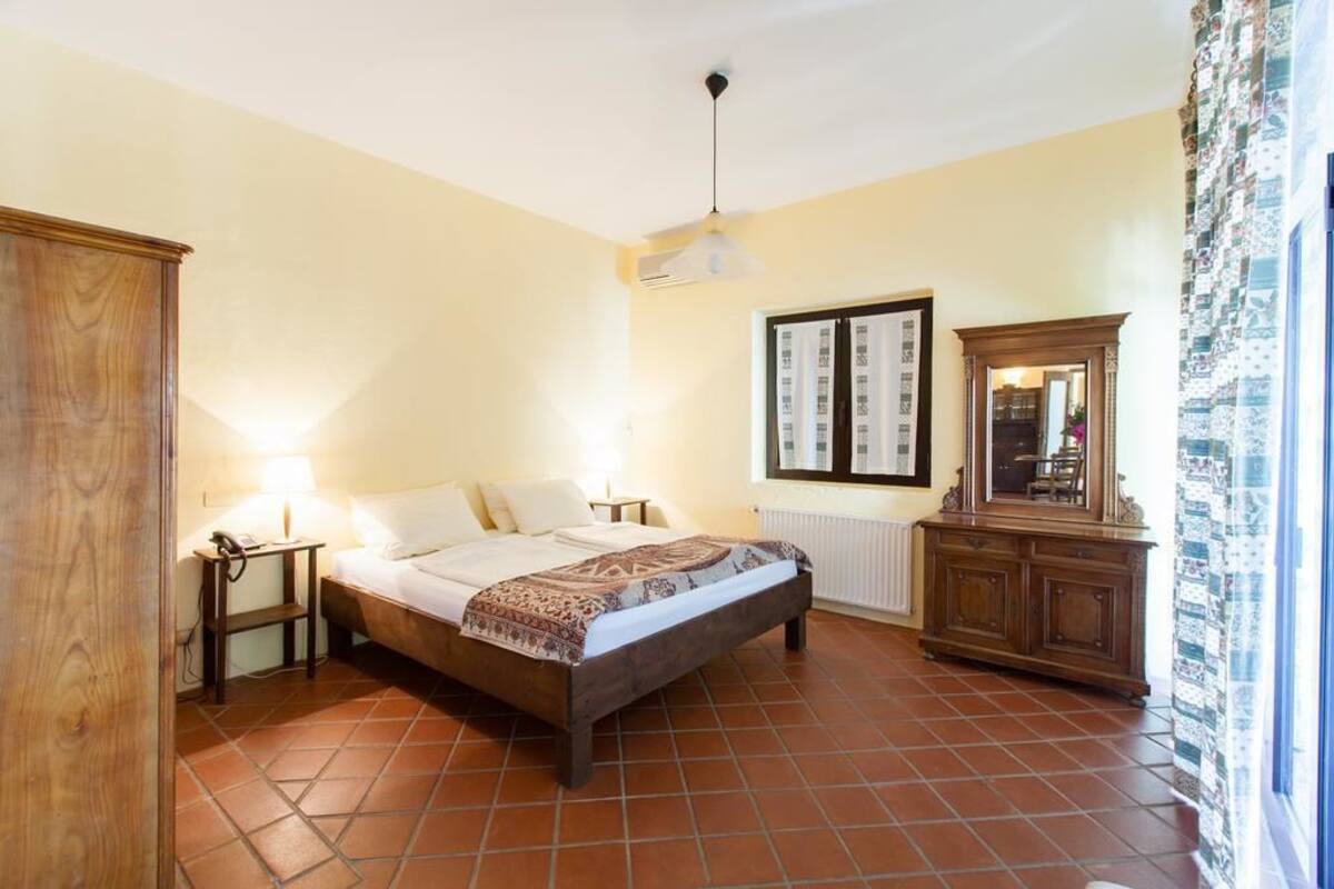 A bedroom with a bed, bedside lamps, a wooden wardrobe, a radiator, and a mirror.