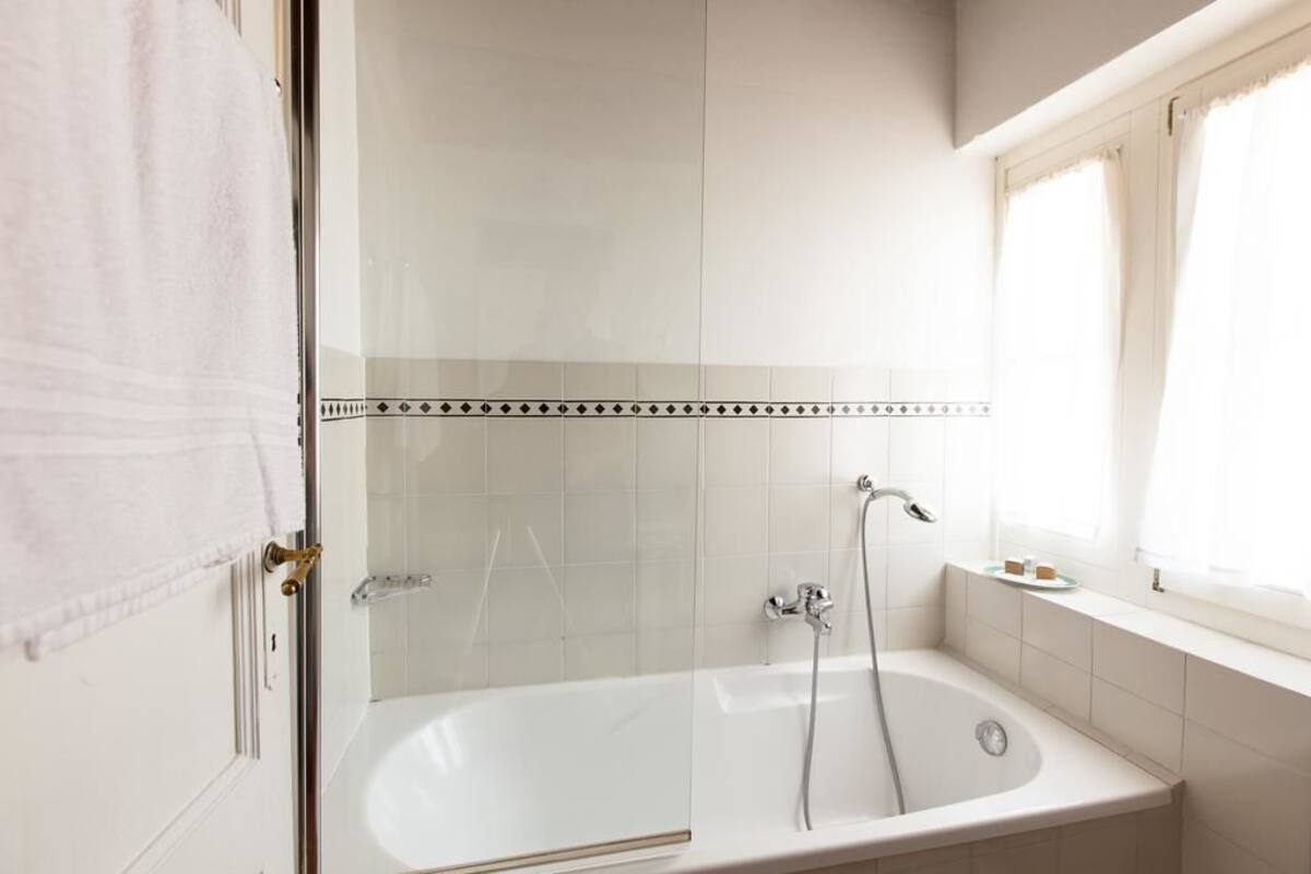 A bathroom with a bathtub, a shower, and a window with curtains.
