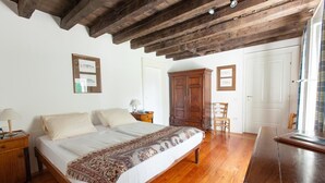 A bedroom with a large bed, wooden floor, and a ceiling with exposed beams. There is a wardrobe, a chair, and a desk with a lamp. - Villa di Tissano (Santa Maria la Longa)