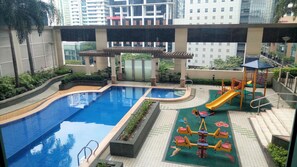 Relax by the rectangular pool surrounded by a deck and a children's play area with a slide and a seesaw.