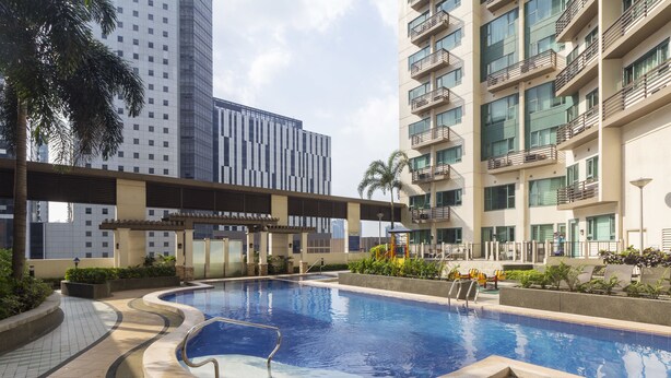 Una piscina con bordo piastrellato, circondata dal verde e con edifici moderni sullo sfondo.