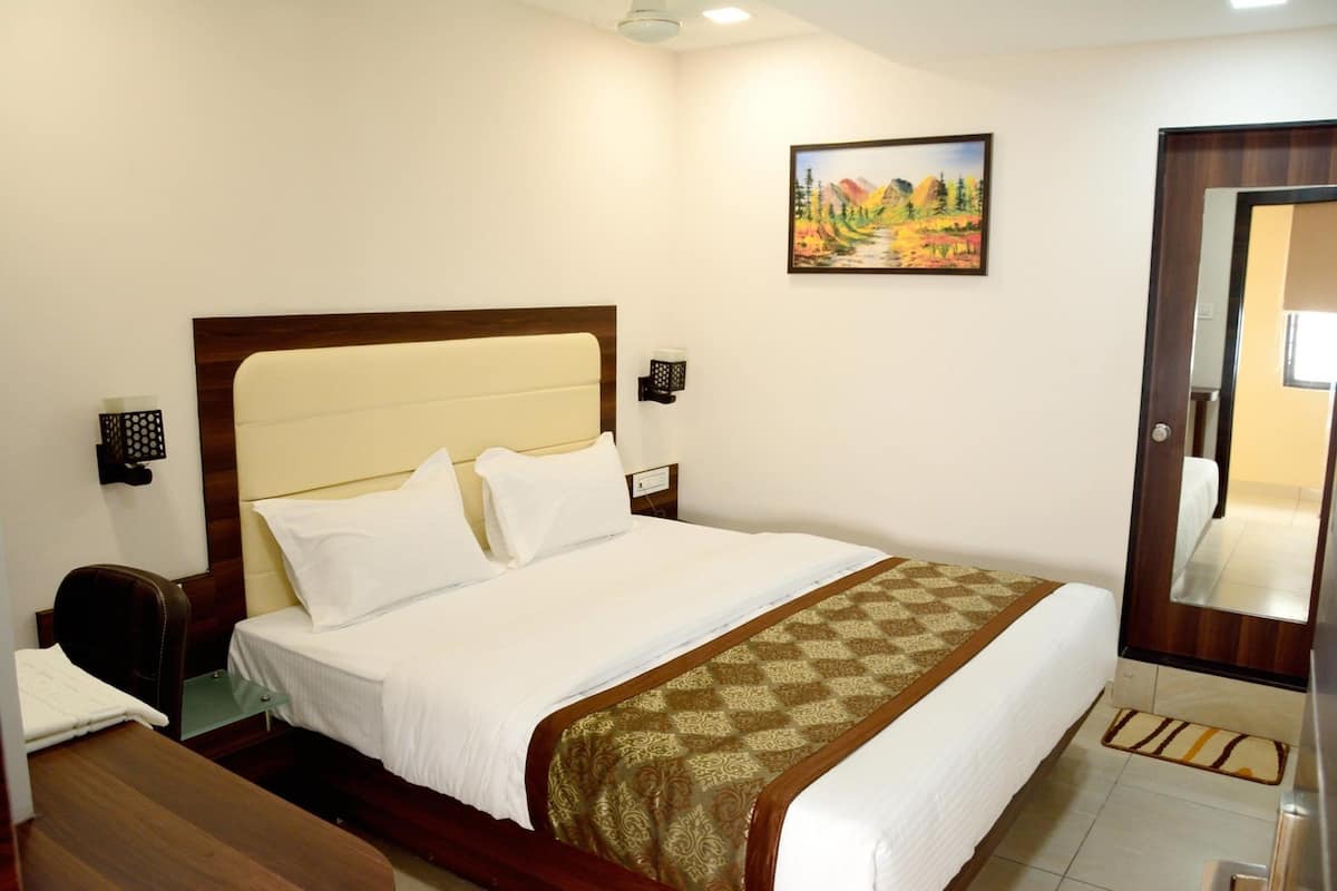 A hotel room with a large bed, a desk, a chair, a nightstand, a wall-mounted lamp, and a painting on the wall.