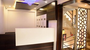 A reception area with a modern design, including a reception desk, a staircase with a decorative glass partition, and a ceiling with recessed lighting.