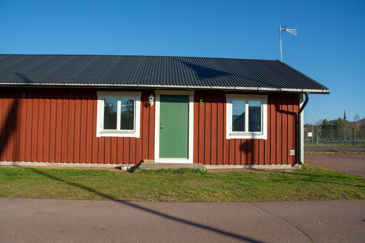 A red building with a green door, white-framed windows, and a metal roof.