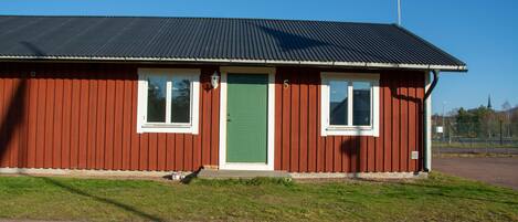 A red building with a green door, white-framed windows, and a metal roof.
