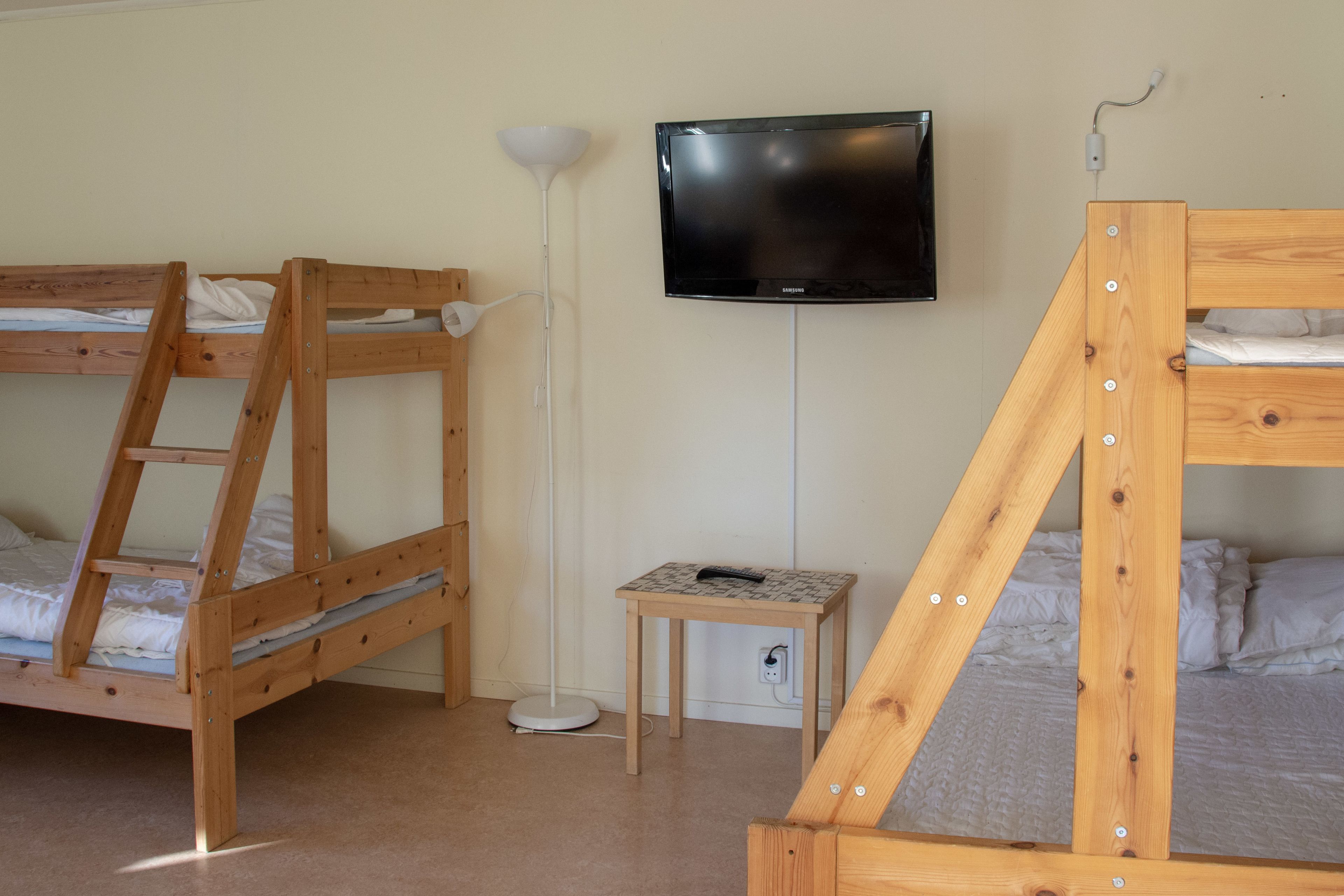 Ein Zimmer mit zwei Etagenbetten, einem an der Wand befestigten Fernseher und einem kleinen Tisch mit einer Fernbedienung.