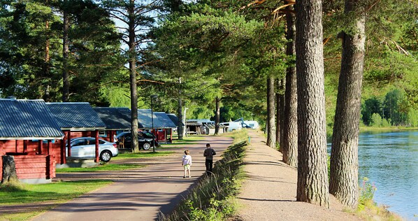 A lakeside path with cabins and a car parked nearby.
