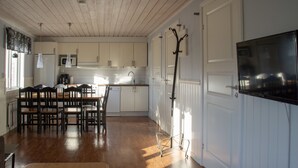Eine geräumige Küche mit Holzboden, weißen Schränken, einem Essbereich mit Stühlen und einem an der Wand befestigten Fernseher.