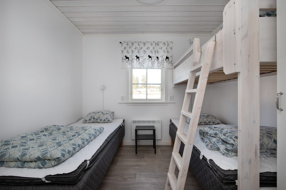 A small, clean room with two bunk beds, a window with a floral curtain, and a small table.