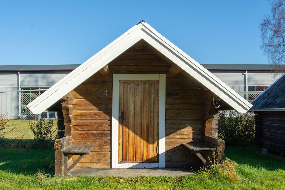 A small wooden cabin with a pitched roof, a wooden door, and two benches outside.