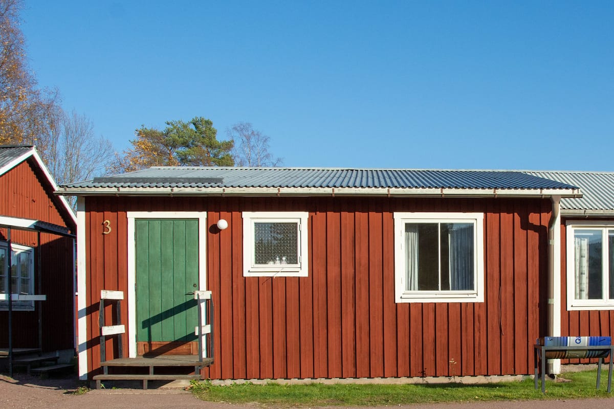 A red wooden building with a green door, two windows, and a small porch.