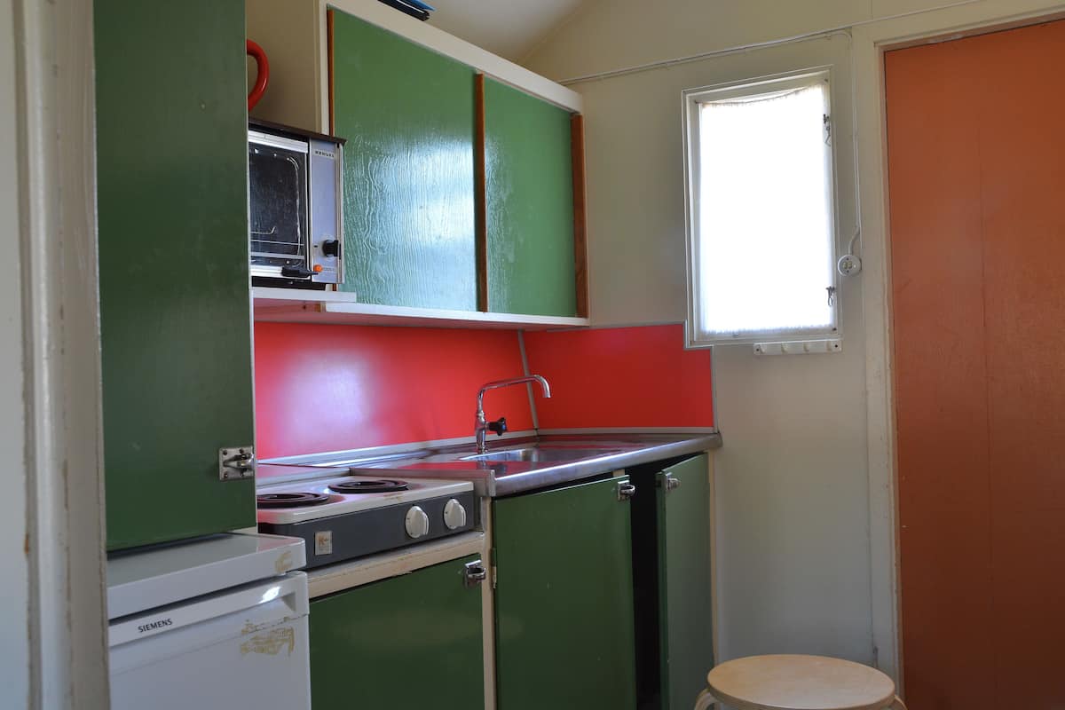 A compact kitchen with green cabinets, a white refrigerator, and a window with a white blind.