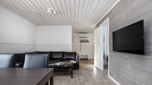 Ein modernes Wohnzimmer mit einem dunkelbraunen Ledersofa, einem Holzesstisch und einem großen Flachbildfernseher, der an einer Holzwand angebracht ist.