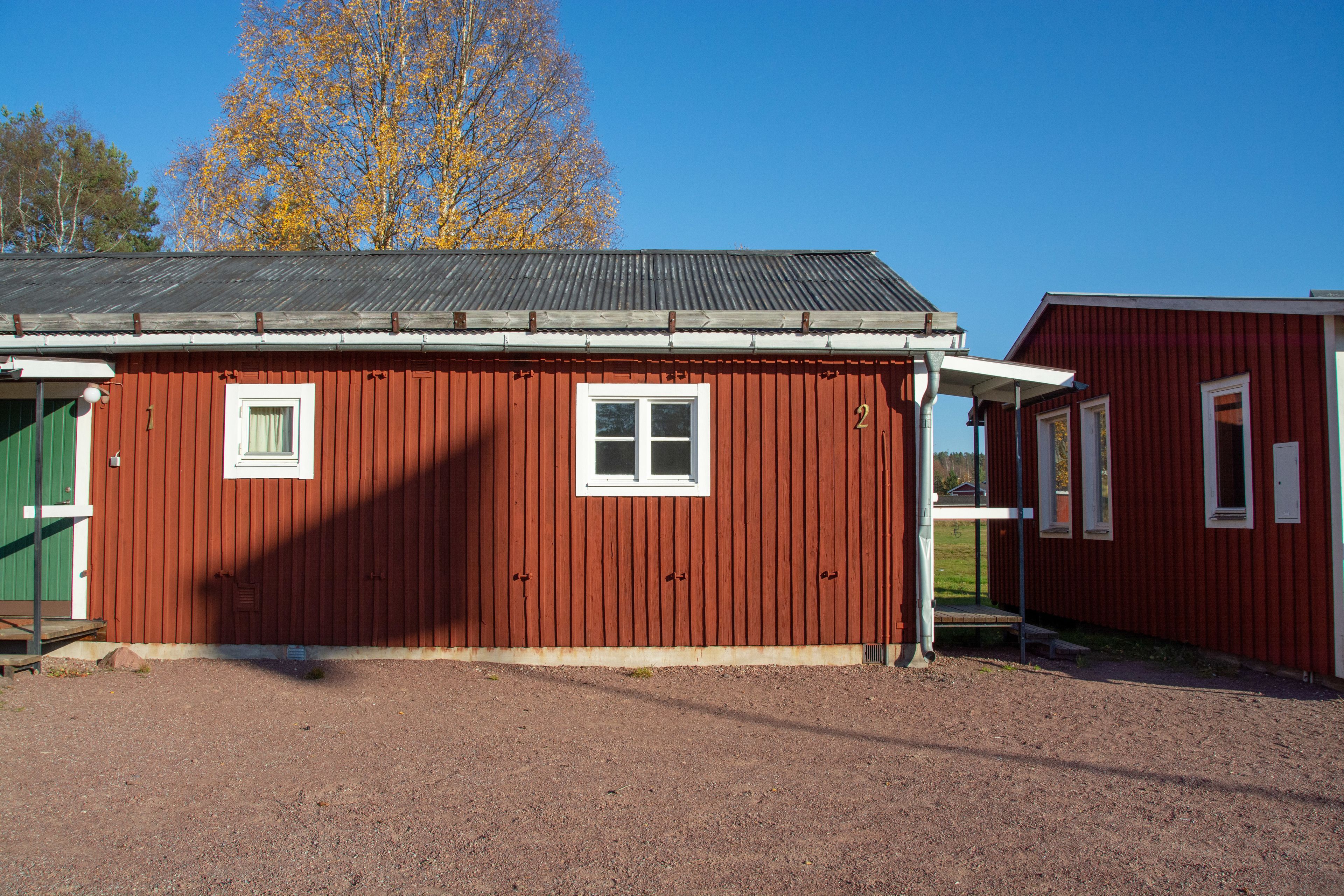 A red wooden building with a metal roof, a green door, and a window.