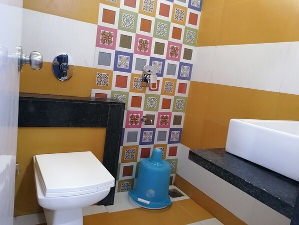 A small bathroom with a white toilet, a blue water dispenser, and a tiled wall with a checkered pattern. - Hotel Laabh (Diu)