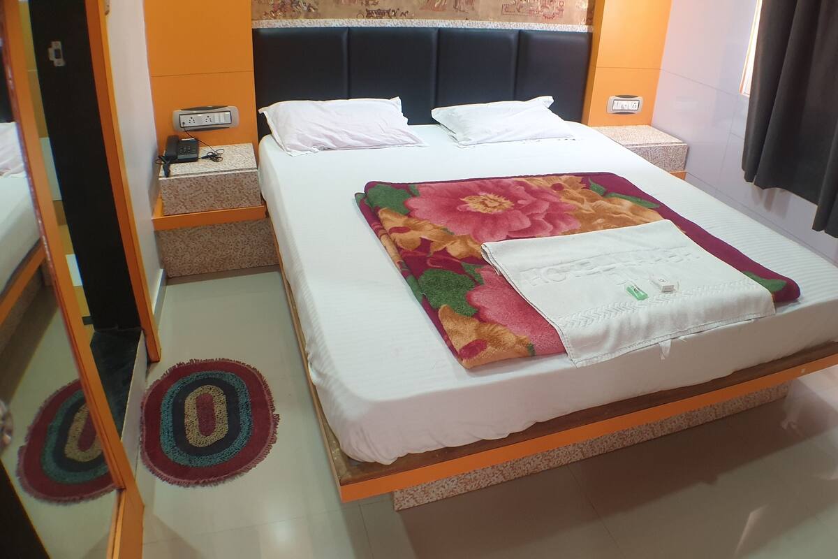 A hotel room with a bed, a nightstand, a power outlet, and a wall socket.