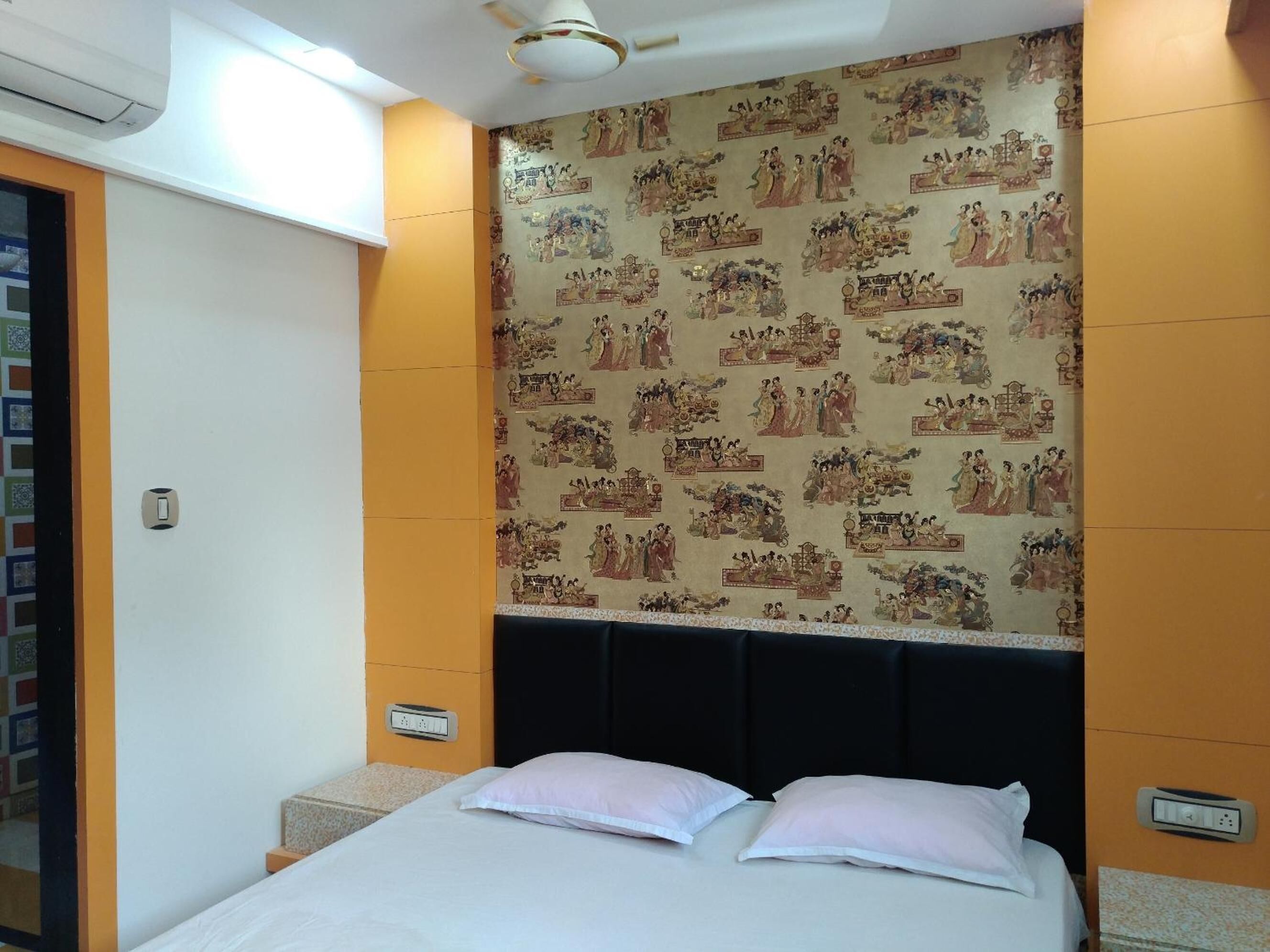 Quarto de hotel com cama, cabeceira, parede com arte tradicional e ventilador de teto.