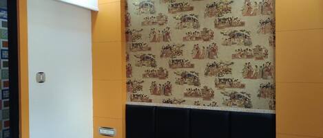 Quarto de hotel com cama, cabeceira, parede com arte tradicional e ventilador de teto.