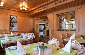 A restaurant with wooden paneling, tables set with white napkins and silverware, and a chandelier. - Gasthof Hotel Hirschen (Schluchsee)