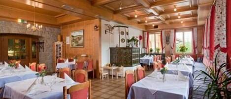 A restaurant with wooden ceiling beams, multiple tables with white tablecloths, and red chairs.
