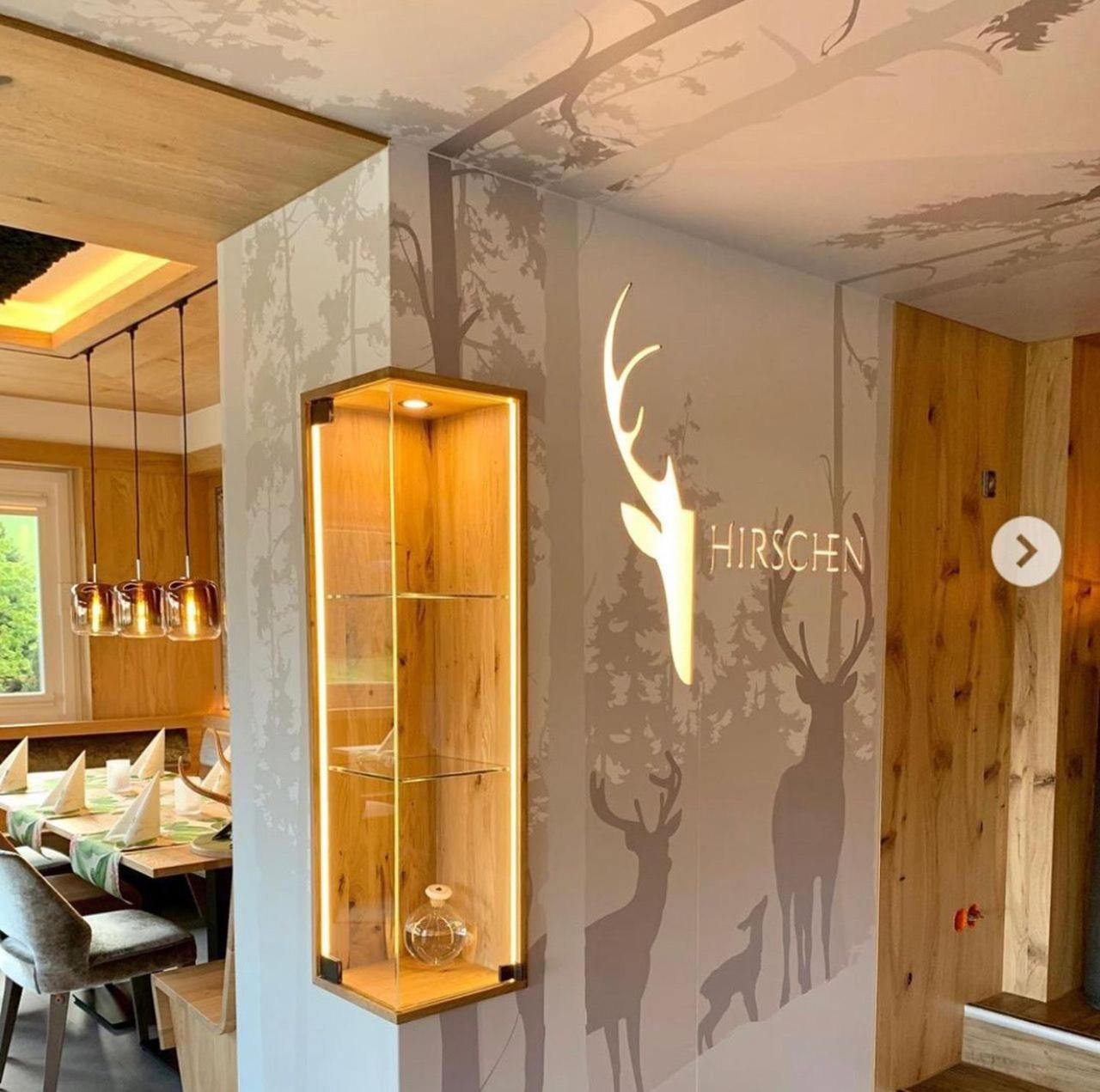 Un intérieur moderne avec un mur en bois et une vitrine, un coin repas avec des tables et des chaises, et une silhouette de cerf fixée au mur.