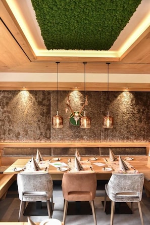 Un espace de salle à manger moderne avec une table en bois, des chaises à revêtement gris et un mur vert orné d’un motif texturé.