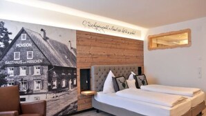 A modern hotel room with a large bed, a small seating area, and a mural of a building. - Gasthof Hotel Hirschen (Schluchsee)