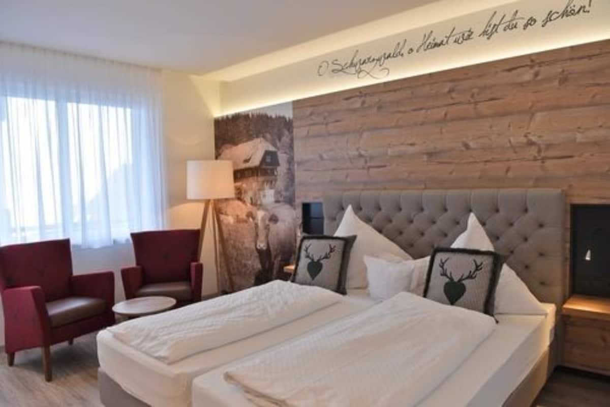 A hotel room with a large bed, two red armchairs, a round table, and a wooden wall with a mural.