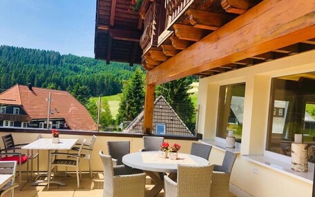 An outdoor patio with a round table and wicker chairs, overlooking a forested valley.