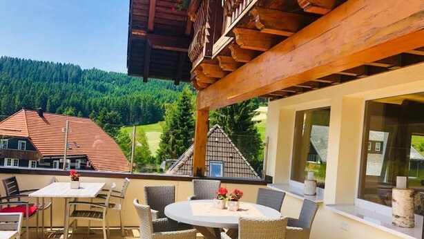 An outdoor patio with a round table and wicker chairs, overlooking a forested valley. - Gasthof Hotel Hirschen (Schluchsee)