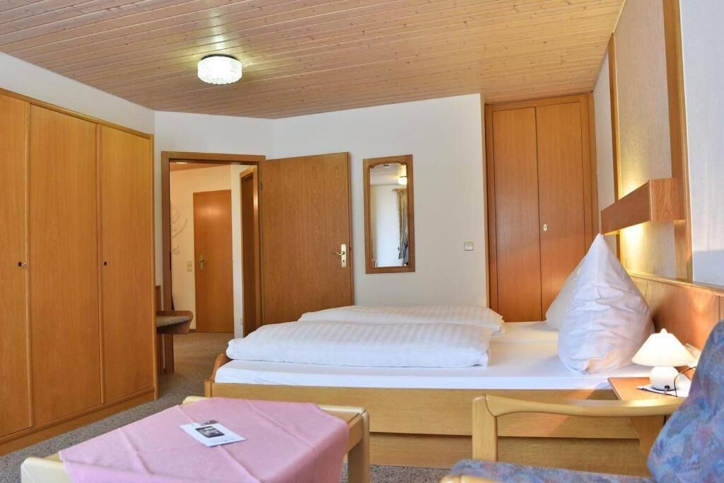 Ein Hotelzimmer mit Holzbalkendecke, einem Bett mit weißer Bettwäsche, einem Nachttisch mit Lampe und einem Sessel.
