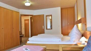 Ein Hotelzimmer mit Holzbalkendecke, einem Bett mit weißer Bettwäsche, einem Nachttisch mit Lampe und einem Sessel.
