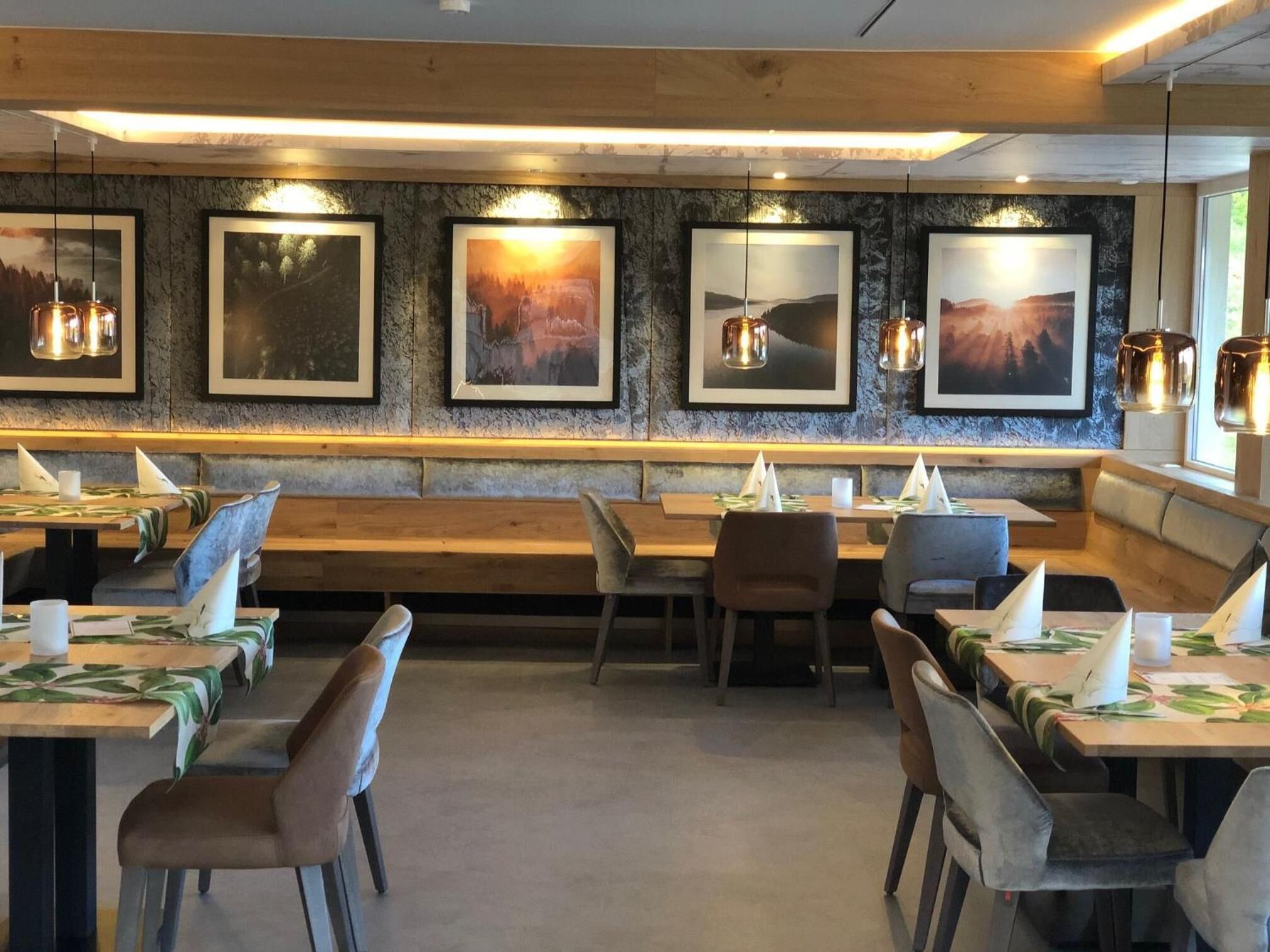 A restaurant with wooden benches and tables, framed pictures on the wall, and pendant lighting.