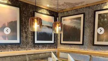 A dining area with a wooden table, cushioned chairs, and framed landscape pictures on the walls.