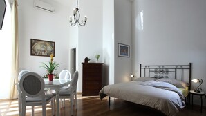 A bedroom with a bed, bedside table, lamp, and a dining area with chairs and a table. - Napolipietrasanta LT (Naples)
