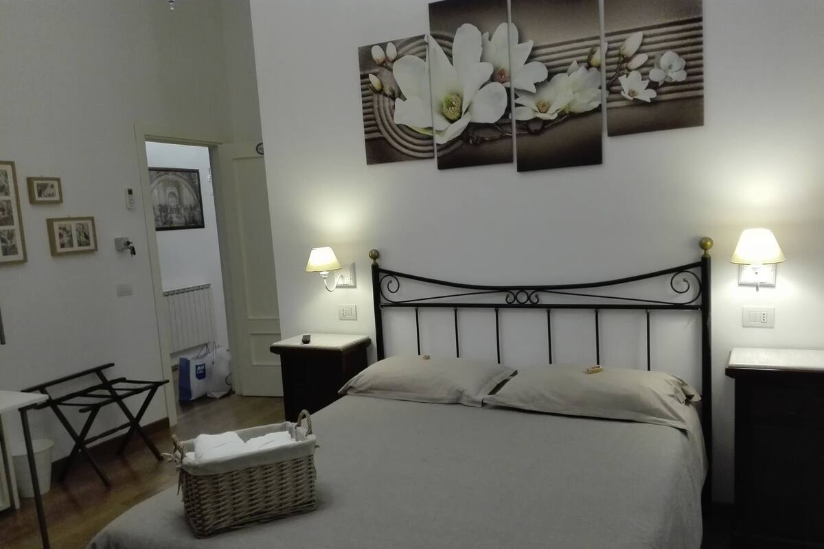 A neatly arranged bedroom with a bed, bedside tables, a lamp, and a wall-mounted artwork.